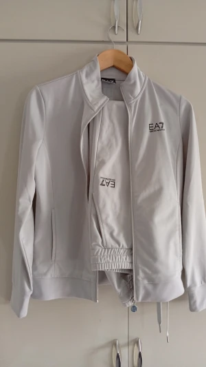 EA7 Dress  - Snygg vit dress från EA7 Emporio Armani med hög krage och dragkedja framtill. Tröjan har logga på bröstet och längs ryggen, samt ribbade muddar och dragsko i nederkant. Tillverkad i ett mjukt och stretchigt material som känns sportigt.