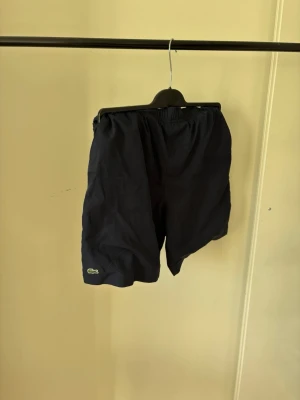 Mörkblå shorts från Lacoste - Snygga svarta skorts från Lacoste med elastisk midja och diskret logga på benet. Tillverkade i ett lätt och bekvämt material som passar perfekt för en avslappnad stil. Klassisk och enkel design som är lätt att matcha.