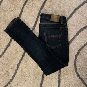 Mörkblå nudie jeans - Ett mörkblått par nudie jeans. I extremt bra skick med lite snygg fading, storlek 30/32 men är väldigt slim. Fickorna är lite noppriga. Har ett litet märke ifrån att ett hål lagades men inget som märks om man inte vet om det