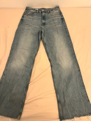 Blåa vida jeans med rå kant - Ett par ljusblå jeans med breda ben och råa, fransiga benslut. Klassisk femficksmodell med hög midja och slitna detaljer för en avslappnad look. Perfekta för dig som gillar en trendig och bekväm stil.