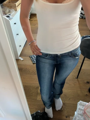 Blå bootcut jeans med slitningar - Säljer ett par klassiska blå jeans med bootcut ben och snygga slitningar. Jeansen har 4 fickor, normal midja och dragkedja med knapp. Materialet är denim i bomull och de har en lätt tvättad look som ger en avslappnad stil.