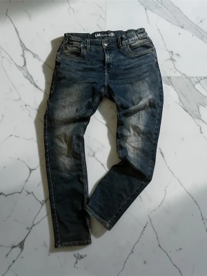 Lab industries Jeans - LAB Industries jeans i blå tvätt, storlek 170. Smal passform i klassisk 5-pocketmodell. Använt skick med tvättslitage och veck som syns på bilderna. Säljes som de är.