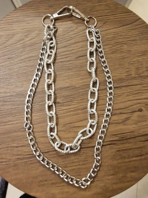 Dubbel byxkedja i silverfärg - Säljer en byxkedja dubbel kedja i silverfärg med två olika länkmönster. Ena kedjan har större, ovala länkar medan den andra är något tunnare och mer klassisk. Perfekt som accessoar till streetwear eller för att ge din outfit en edgy touch.