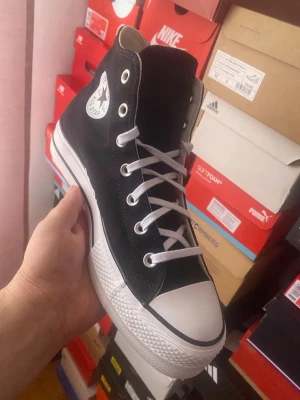 Svarta Converse Chuck Taylor Highs - Klassiska svarta Converse Chuck Taylor All Star med högt skaft. Skorna har vit tåhätta i gummi, vita snören och metallöljetter. Den ikoniska loggan sitter på sidan och sulan är vit med svart rand. Ovandelen är i canvas vilket ger en tidlös och clean look.