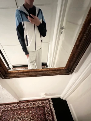 DIF vindjacka - Snygg vindjacka från Djurgårdens IF i ljusblått, vitt och mörkblått. Jackan har dragkedja framtill, huva och klubbens broderade märke till höger. Tillverkad i lätt och vindtätt material.