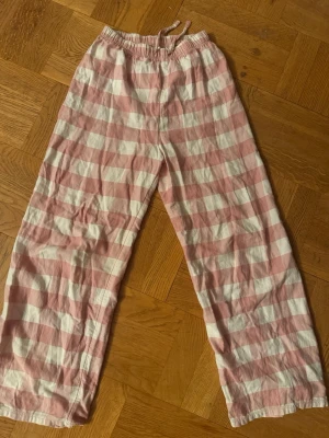 Randiga pyjamasbyxor från H&M - Säljer ett par pyjamasbyxor från H&M i mjuk bomull med breda rosa och vita ränder. Byxorna har resår i midjan och dragsko för extra komfort. Perfekta för mysiga hemmakvällar eller lata morgnar.