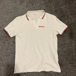 Vit pikétröja från Prada - Säljer en stilren vit pikétröja från Prada med klassisk krage och knappar. Nypris ligger på 3000+, jag säljer för 650