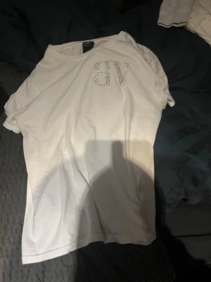Vit Bvaldi t-shirt - Vit t-shirt med rund hals och korta ärmar. På bröstet står det 'VB' i strass och på ryggen står det 'NEED MONEY FOR PORSCHE' i samma stil. T-shirten har en avslappnad passform och är gjord i mjukt bomullsmaterial.
