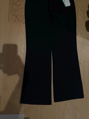 Svarta utsvängda jeans - Säljer ett par svarta jeans med utsvängda ben och super låg midja. Jeansen har en bakficka med lock och knappdetalj. Perfekta för dig som gillar en trendig och avslappnad stil. Har prislapparna på och har aldrig varit användna! 