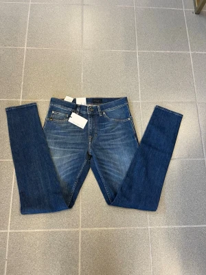 Blå slim fit jeans från tiger of sweden W30 L34 - Snygga blå slim fit jeans från tiger of sweden med klassisk femficksdesign och subtila slitningar framtill. Jeansen har normal midja, raka ben och är tillverkade i mjuk denim med stretch för extra komfort.