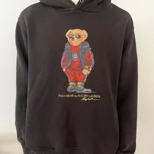 Polo Bear hoodie - Svart hoodie från Polo Ralph Lauren med ikoniskt Polo Bear-tryck på bröstet. Tröjan har huva, ribbade muddar och en avslappnad passform. Tillverkad i mjuk bomull, perfekt för en chill och stilren look. Hör av dig vid funderingar!