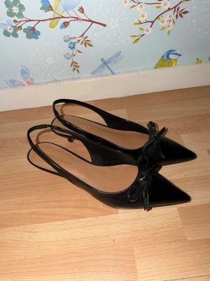 Svarta slingback-pumps med rosett - Stilrena svarta pumps från Anna Field med spetsig tå, låg klack och öppen häl med slingback-rem. Skorna har en elegant rosett framtill och är tillverkade i ett glansigt material som ger en lyxig känsla. Perfekta för att lyfta vilken outfit som helst.💕