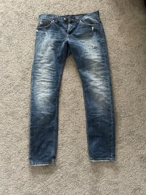 Dondup jeans  - Säljer ett par blå jeans med slitningar och tvättade detaljer. Jeansen har raka ben, klassisk femficksmodell och knappgylf. Materialet är denim i bomull och de har en cool, avslappnad look med distressed effekter.