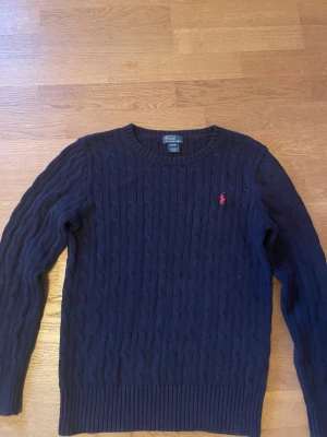 Ralph Lauren Kabelstickad Tröja - Mörkblå Ralph Lauren kabelstickad tjocktröja. Storlek:L. Mycket bra skick. Priset ej hugget i sten vid en snabb affär! Skickar alltid inom 1 dag! Tveka inte att höra av dig vid minsta fråga!