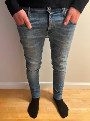 Blå anbass jeans från Replay - Säljer ett par blå skinny jeans från Replay med klassisk femficksmodell och snygga slitningar. Jeansen har en smal passform och är tillverkade i stretchigt denimtyg för extra komfort. Perfekta för dig som gillar en modern och tajt look.