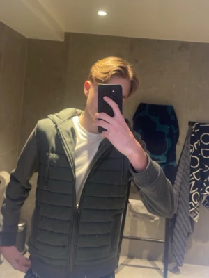 Grå quiltad hoodie-cardigan - Snygg grågrön hoodie-cardigan med quiltade partier framtill och på ryggen. Dragkedja hela vägen, två fickor och ribbade muddar. Huva med dragsko för extra stilpoäng. Perfekt till chill eller streetwear-look. Hör av er!