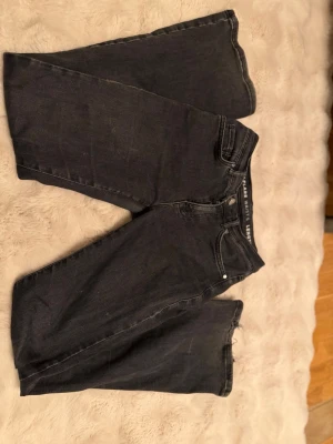 Svarta low flare jeans - Säljer ett par svarta low flare jeans med utsvängda ben och låg midja. Jeansen har klassisk femficksdesign och silverfärgade nitar. Längd 31. Perfekta för en trendig och avslappnad stil. Lite slitningar på ena sidan av byxan men inte mycket
