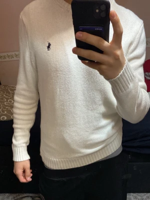 Vit stickad tröja från Ralph Lauren - Säljer en stilren vit stickad tröja från Ralph Lauren med den klassiska broderade loggan på bröstet. Tröjan har rund halsringning, långa ärmar och ribbade muddar vid ärmslut och nederkant. Perfekt för en clean och enkel look.