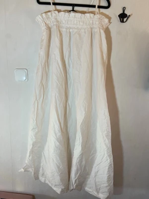 Vit långklänning med tunna band - Luftig vit långklänning med smala axelband och smockad överdel. Klänningen har en rak, flowy passform och är tillverkad i ett lätt tyg som passar perfekt för varma dagar. Sommarklänning/strandklänning. Enkel och stilren design utan mönster eller extra detaljer. Fint skick, inga skavanker. Lager 157, storlek M. Djur, rök och parfymfritt hem.