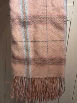 Rutig rosa halsduk - Mysig halsduk i mjukt material från Ally. Den är ljusrosa med rutigt mönster, samt har fransar i ändarna. Perfekt accessoar för att addera färg till din outfit. Ny (aldrig använt)