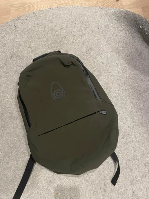 Olivgrön ryggsäck från sail racing  - Snygg olivgrön ryggsäck från sail racing  med minimalistisk design och svarta detaljer. Ryggsäcken har en frontficka med dragkedja, vadderade axelband och ett stilrent logotryck. Tillverkad i slitstarkt material som passar perfekt för skolan eller stan.