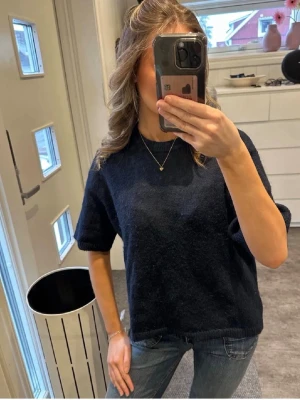 Mörkblå stickad topp - Mysig mörkblå stickad topp med korta ärmar och rund hals. Perfekt till jeans och enkel att styla med smycken. Materialet känns mjukt och ger en avslappnad men ändå snygg look.