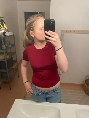 Mörkröd tight t-shirt - Säljer en mörkröd, tight t-shirt med korta ärmar och rund hals. T-shirten är enkel och stilren, perfekt till jeans eller kjol. Materialet känns mjukt och stretchigt, troligtvis bomull eller en bomullsblandning. Inga synliga tryck eller detaljer.