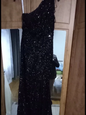 Svart glittrig långklänning oneshoulder - Säljer en svart långklänning med glittriga paljetter och oneshoulder-design. Klänningen har en hög slits framtill och sitter figurnära. Perfekt för dig som vill sticka ut på festen med en elegant och trendig look.
