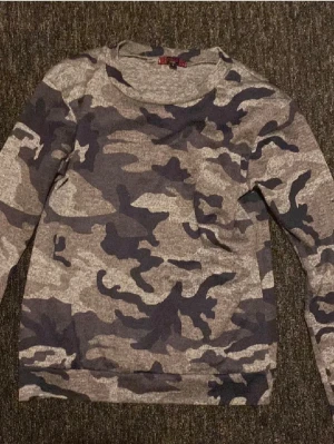 Camo mönstrad sweatshirt - Säljer en långärmad sweatshirt med camo-mönster i olika nyanser av grått och svart. Tröjan har rund halsringning och är tillverkad i mjukt material, perfekt för en avslappnad streetwear-look.