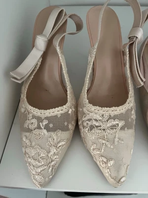 Beige spetsiga pumps med rosett - Säljer ett par eleganta pumps i beige med spetsdetaljer och blommigt broderi. Skorna har spetsig tå och fina band som knyts till rosett runt ankeln. Använd fåtal gånger så inga märken! kontakta vid frågor eller köp direkt😊💞