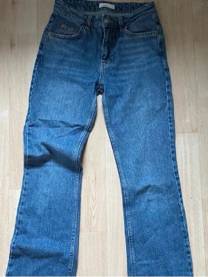 Blå raka jeans medelhög midja - Säljer ett par klassiska blå jeans med bootcut och medelhög midja. Jeansen har fem fickor, knappgylf och är tillverkade i ett slitstarkt denimtyg. Perfekta för en avslappnad och trendig look.
