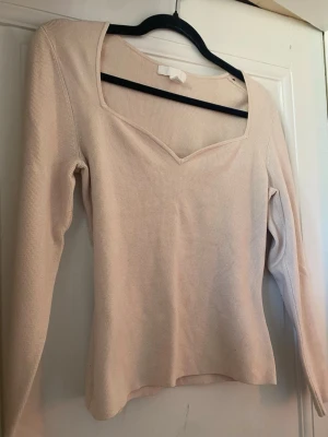 Beige ribbad topp med v-ringning H&M❣️❣️ - Säljer en beige ribbad topp från H&M med lång ärm och snygg v-ringad hals. Toppen har en mjuk, stretchig känsla och sitter snyggt på kroppen. Perfekt att styla med jeans eller kjol för en clean look.