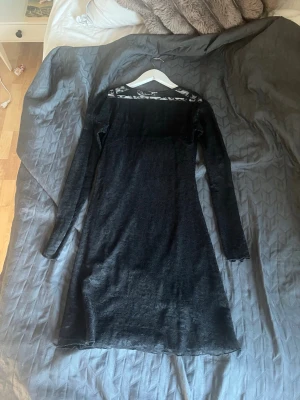 Svart långärmad klänning med spets från h&m  - En svart långärmad klänning med transparent spetsdetalj upptill vid halsen. Klänningen har en rak passform och är tillverkad i ett mjukt, stretchigt material som ger en bekväm känsla. Perfekt för dig som gillar stilrena och eleganta plagg. Är i storlek 158/164💓💓