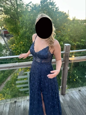 Marinblå långklänning med spetsdetaljer - Elegant marinblå långklänning med tunna axelband och v-ringning. Klänningen har spetsdetaljer och transparent midjeparti samt ett subtilt bladmönster över hela tyget. Kjolen har en slits framtill som ger en snygg touch. Perfekt för speciella tillfällen. Nypris är 1700kr, måtten är byst: 97cm, midja: 79cm, höfter: 105cm