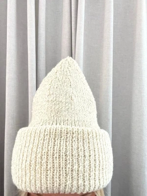 Vit stickad mössa med uppvikt kant i reflexgarn - Handstickad vit mössa med hög, uppvikt kant, liknande den populära ”Acne” modellen🤍 Mössan är gjord i tjockt garn med reflextråd som gör en synlig i mörker✨Perfekt för dig som vill synas och ha en unik accessoar till vintern.🤍🤍