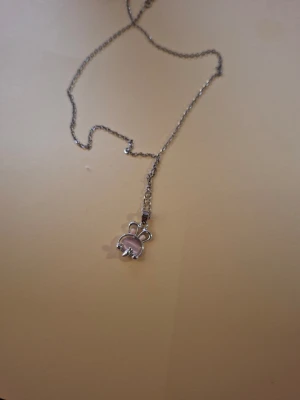 Silverhalsband med rosa nallehänge - Sött halsband i silverfärg med ett litet nalleformat hänge. Hänget har detaljer i ljusrosa och vitt, vilket ger en gullig och lekfull look. Kedjan är tunn och smidig, perfekt för dig som gillar söta accessoarer med en personlig touch.