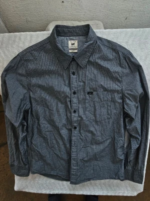 Randig skjorta från Lee i bomull - Snygg mörkblå skjorta från Lee med tunna vita ränder och klassisk krage. Skjortan har lång ärm, bröstficka och knappar framtill. Slim fit-modell i mjuk bomull som passar perfekt till jeans eller chinos.