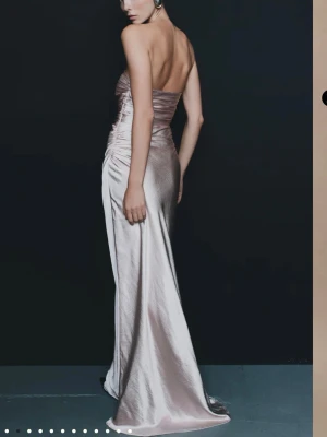 Champagnefärgad axelbandslös långklänning - Elegant axelbandslös långklänning i skimrande champagnefärgad/rosa satin. Klänningen har figurnära passform med lätt rynkade detaljer i sidorna och slät, svepande kjol. Köpte till min bal men var tyvärr lite för liten för mig! Jätte lyxig i matrialet samt med lyxig ”tygd”. Är 167 och den är väldigt lång på mig samt lång med klackar! Har M/S i vanliga fall🥰🥰😇Pris går absolut att diskutera! Köpte för nypris för €109,00 ≈ 1176 kr samt frakt på 250kr samt tull på de så allt som allt blev 1800kr