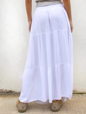 Vit långkjol i bomull - Säljer en flowy vit långkjol med flera volanger och resår i midjan. Kjolen är tillverkad i ett tunt och luftigt bomullstyg, perfekt för varma dagar. 