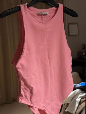Rosa body från Zara - Säljer en enkel och snygg rosa body från Zara. Bodyn har ärmlös design, rund halsringning och är gjord i ett mjukt, stretchigt material som sitter skönt mot kroppen. Perfekt att styla med jeans eller kjol för en trendig look.
