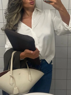 Vit sidenliknande skjorta från Zara - Stilren vit skjorta från Zara i ett glansigt, sidenliknande material. Skjortan har klassisk krage, långa ärmar och en avslappnad passform. Perfekt att styla till jeans eller kjol för en clean look.