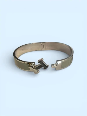  H Click armband khaki - Snyggt H Click armband i metall med khakigröna emaljdetaljer och ikoniskt H-spänne framtill. Armbandet har en stilren och modern design som passar perfekt till din accessoarsamling. Metallfinishen ger en exklusiv känsla och färgen är lätt att matcha.