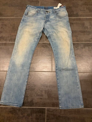 Ljusblå jeans från Armani Jeans - Säljer ett par ljusblå jeans från Armani Jeans med klassisk femficksmodell och raka ben. Jeansen har slitna detaljer och gul kontrastsöm. Perfekta för dig som gillar en avslappnad och trendig look. 