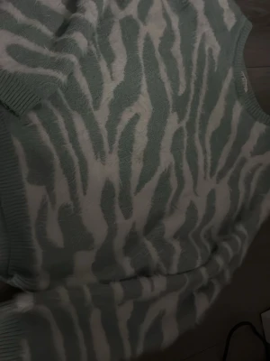 Grönvit zebramönstrad stickad tröja - Mysig stickad tröja från H&M i ljusgrönt och vitt med zebramönster. Tröjan har rund halsringning och ribbade muddar vid ärmslut och nederkant. 