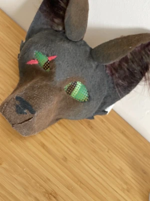 Handgjord vargmask cosplay - Unik handgjord vargmask för cosplay eller maskerad. Masken är gjord i grått och brunt tyg med stora spetsiga öron och färgglada detaljer vid ögonen. Nosen är lång och masken har elastiskt band för att sitta på plats. Passar perfekt till djur- eller fantasyutklädnad.