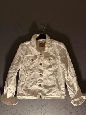 Vit jeansjacka från Sisters Point - Snygg vit jeansjacka från Sisters Point med klassisk krage, knäppning framtill och två bröstfickor med lock. Jackan har raka ärmar och en stilren look som passar perfekt till många outfits.