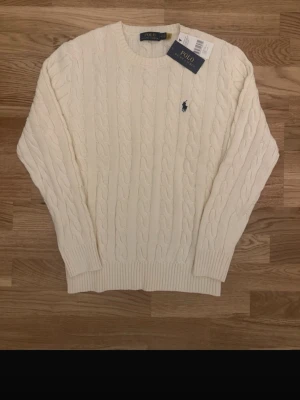 Vit/begie kabelstickad tröja Polo Ralph Lauren - Kabelstickad vit/beige tröja från Polo Ralph Lauren. Klassisk kabelstickad tröja från Polo Ralph Lauren i beige färg. Tidlös modell med broderad logga på bröstet. Helt ny med tags, aldrig använd. Kostar 650kr men om man köper den gråa kan man få båda för 1000kr