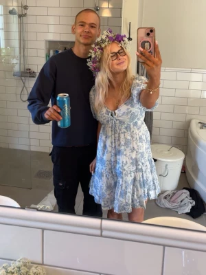 Blåvit blommig kortklänning med puffärm - Söt kortklänning i blått och vitt med blommigt mönster och puffärmar. Klänningen har en v-ringning med knyt framtill och volang sop nederkanten. Perfekt för sommarens alla tillfällen! Den är använd en gång!’