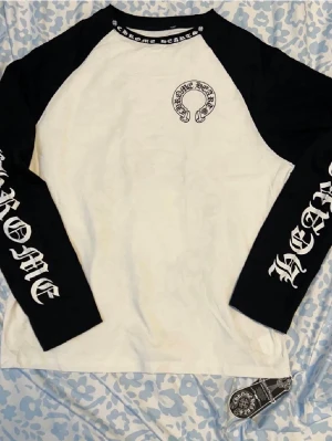Chrome Hearts långärmad t-shirt - Säljer en svartvit långärmad t-shirt från Chrome Hearts med stora logotryck på både fram- och baksida samt på ärmarna. Tröjan har kontrastfärgade svarta ärmar och vit kropp, samt tryck runt halsen. Tillverkad i mjuk bomull för skön passform.