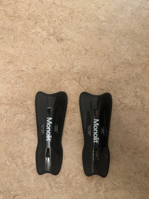 Monolit benskydd i svart kolfiber - Säljer ett par svarta benskydd från Monolit i kolfiber-look. De har en smal, ergonomisk form och är lätta med ventilationshål för extra komfort. Perfekta för dig som vill ha skydd under träning eller match. Kostar 789 men säljer för 300. 14 CM längd